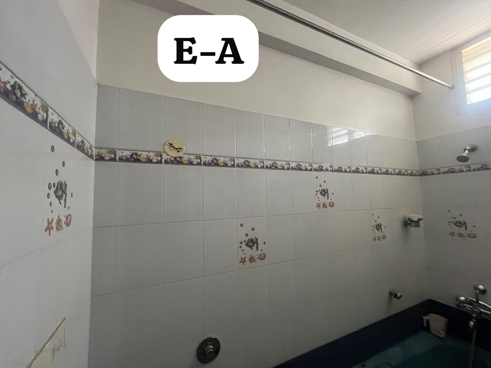 Original bathroom — dated printed border tiles and old shower fittings